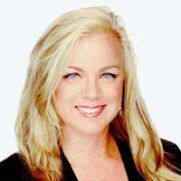 A professional headshot of a woman with long blonde hair, smiling at the camera, wearing a black jacket against a white background.