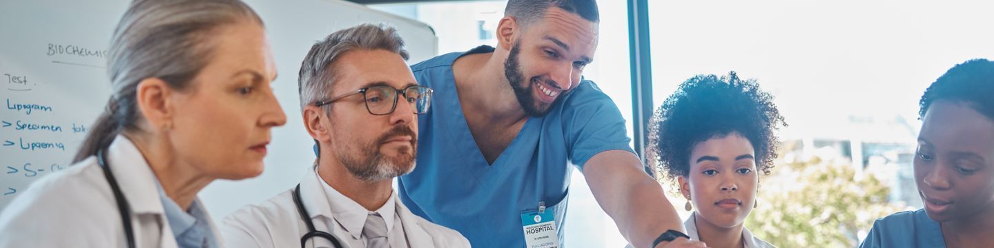 A group of diverse medical professionals, including a nurse and doctors, engage in a collaborative discussion around a whiteboard in a well-lit hospital conference room with no GRE requirement.