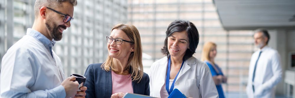 Four professionals conversing in a modern office building's lobby, smiling and exchanging ideas over coffee and documents.